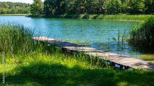 blau grüner See in einer Naturlandschaft mit Bäumen mit hölzernen Steg im Vordergrund