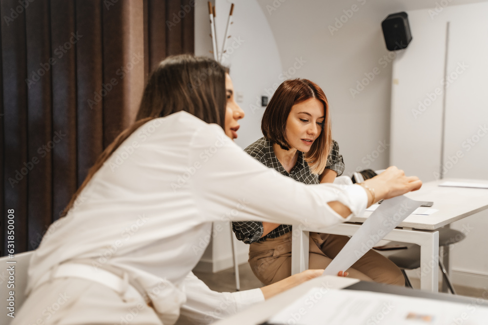 Brunette girl helping her colleague with the test. She is showing her the answer of the question