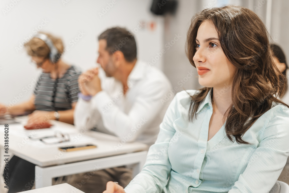 Fototapeta premium Brunette business girl listening to business presentation at the classroom. Stunning female employee smiling while listening to a presentation