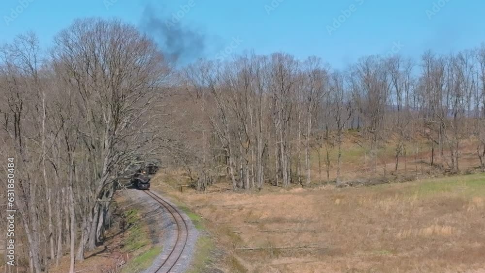 Slow-motion of a steaming train passing between leafless trees and fields during the daytime