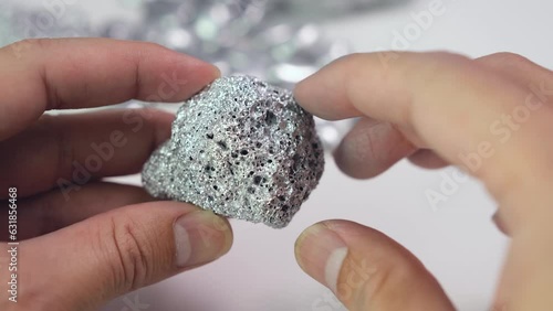 Man's hand holding a lump of silver or platinum or a rare earth mineral on white background	