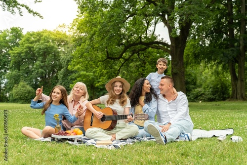Picnic, big family resting on the grass for summer vacation, outdoor recreation and healthy lifestyle together. Grandparents, mother and children with a guitar in a field park © SistersStock
