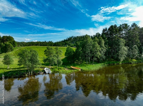 Fototapeta Naklejka Na Ścianę i Meble -  Scenic vista of a tranquil lake surrounded by lush greenery with wooden boats near the shore