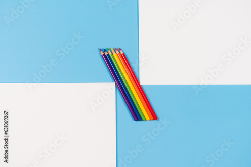 Open white notebooks with purple, blue, green, yellow, orange, red olored pencils on light blue background. Top view, copy space for text photo