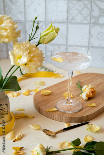 a glass with a cocktail on a long stem on a wooden tray on the kitchen table, next to yellow flowers in a white vase