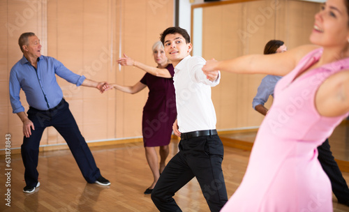 Positive handsome guy dancing lively jive paired with young female partner during group training in dance studio