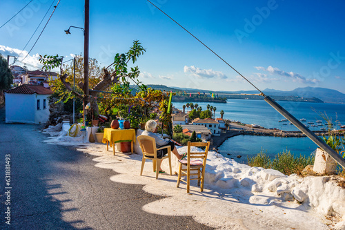 Old woman sitting on a chair gazing the amazing view of Koroni coastal village. Beautiful scenic in Koroni, Greece, Europe.
