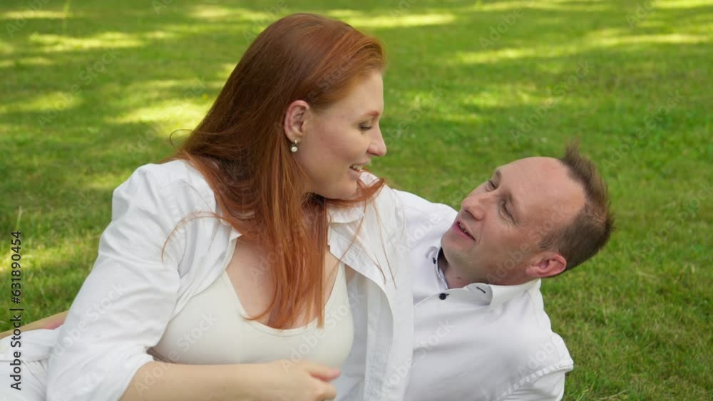 Family day. Pregnant couple embracing lying on green grass in park. Happy parenthood concept. Man hugging and touching woman belly outdoors. Pregnant belly. Love. 4K, UHD Family day. Pregnant couple embracing lying on green grass in park. Happy parenthood concept. Man hugging and touching woman belly outdoors. Pregnant belly. Love. 4K, UHD