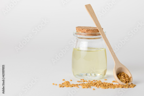 Fenugreek essential oil in glass container  and fenugreek seeds in wooden spoon isolated with copy space