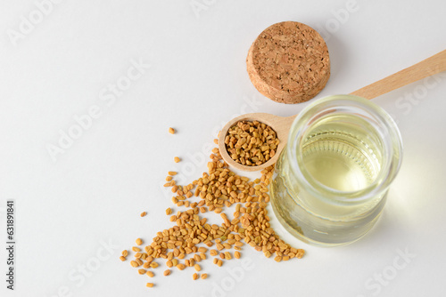 Fenugreek essential oil in open glass container and fenugreek seeds in wooden spoon isolated with copy space