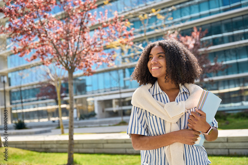 Happy smiling African American girl student standing in university park looking away outdoor dreaming of applying foreign university, study abroad, thinking of admission and scholarship, copy space. photo