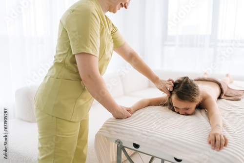 Cropped shot of unrecognizable female pediatric masseuse doing therapeutic massage to relax shoulder joint and shoulder blade of little girl. Kid client get service massage in spa salon.