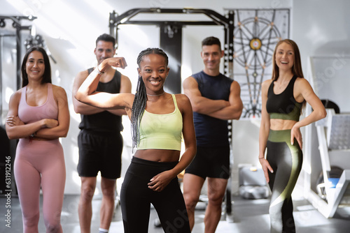 african fitness woman posing with her biceps on camera with a group of fitness friends of different ethnicities