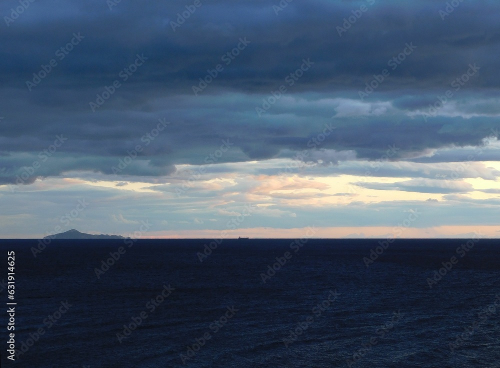 Dark blue sea, clouds, an island and a ship in the background