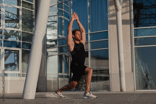 Confidant male athlete doing stretching exercises outdoors against urban building