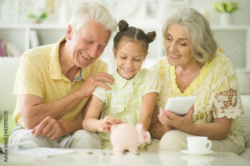 Fotografie Portrait of happy grandparents and grandchild with piggy bank at home