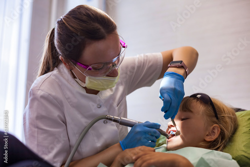 Dentist doctor doing treats teeth little girl 5-6 year old at dental office. Realistic photo of dentist having treating teeth kid girl in clinic. Concept of medical children dentistry. Copy text space