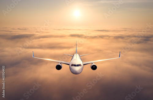Airplane is flying above the clouds at sunset. Landscape with passenger airplane, beautiful clouds, golden sky. Aircraft is taking off. Business travel. Commercial plane. Aerial view of plane