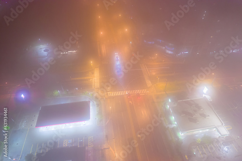 City main intersection at thick foggy night. Cinematic diffusion effect at cars transportation junction activity. Expressway view from above with night lights and illumination.