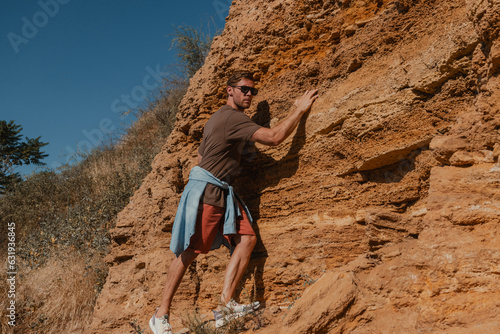 Confident male adventurer holding on grip while climbing the rock as extreme challenge