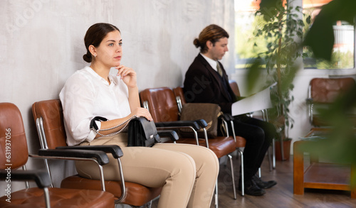 Unemployed young woman sits and waits for invitation to interview. Bored woman candidate with smartphone waiting for invitation to recruiter office