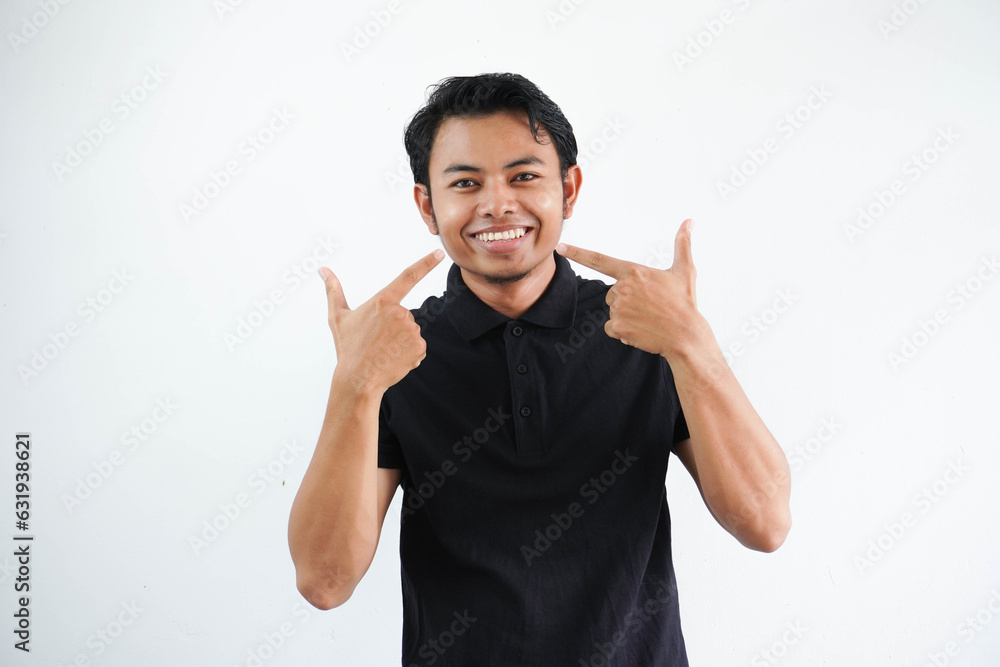 smiling young asian man pointing to his mouth with happy expression wearing black polo t shirt isolated on white background smiling young asian man pointing to his mouth with happy expression wearing black polo t shirt isolated on white background