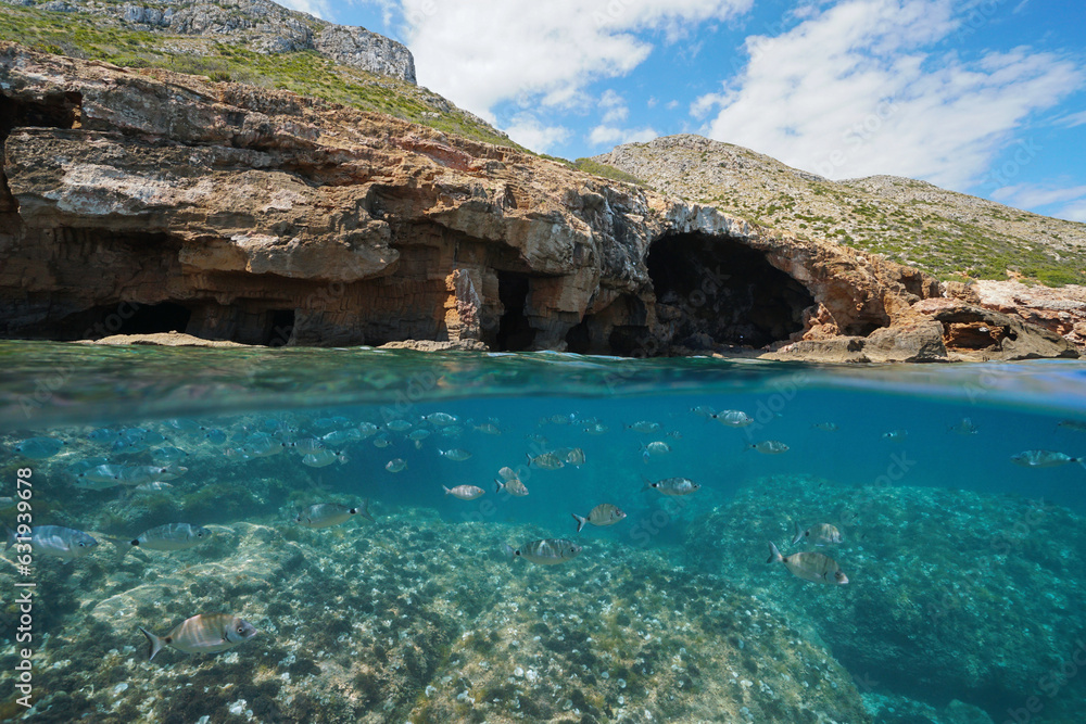 Sea cave on the Mediterranean coast in Spain with a shoal of fish underwater, split view over and under water surface, natural scene, Costa Blanca, Javea, Alicante, Valencia