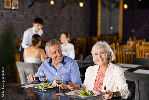 Couple of elderly man and woman having dinner and drinking wine together in restaurant