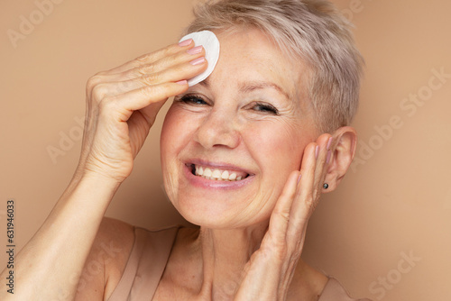 Beautiful elderly 60s woman with short hair doing her everyday routine removing her makeup with cotton pad