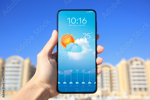 Man using weather forecast app on smartphone outdoors on sunny day, closeup. Data and illustration of sun with cloud on screen