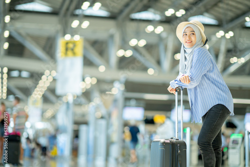 An Asian Muslim wearing a blue hijab is preparing for a vacation and she is at the international airport. She is waiting for her friends, Muslim travelers.