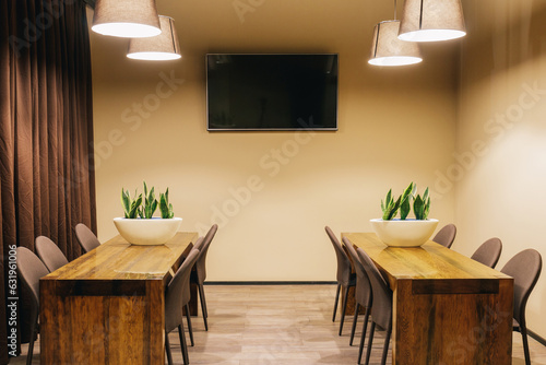 View of the room interior with a wood tables, chairs, brown curtains and tv screen.