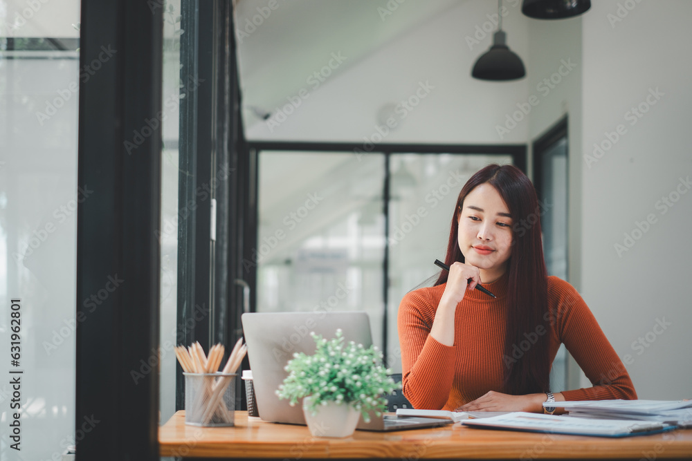 Beautiful Asian woman using laptop and tablet while sitting at her working place. Concentrated at work. Beautiful Asian woman using laptop and tablet while sitting at her working place. Concentrated at work.