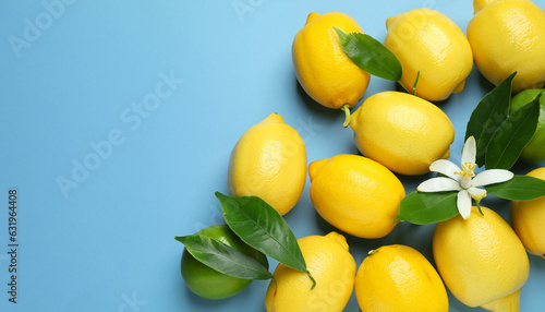 Many fresh ripe lemons with green leaves and flower on light blue background, flat lay. Space for text