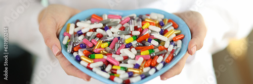 Doctor with stethoscope holds pills in heart-shaped bowl.