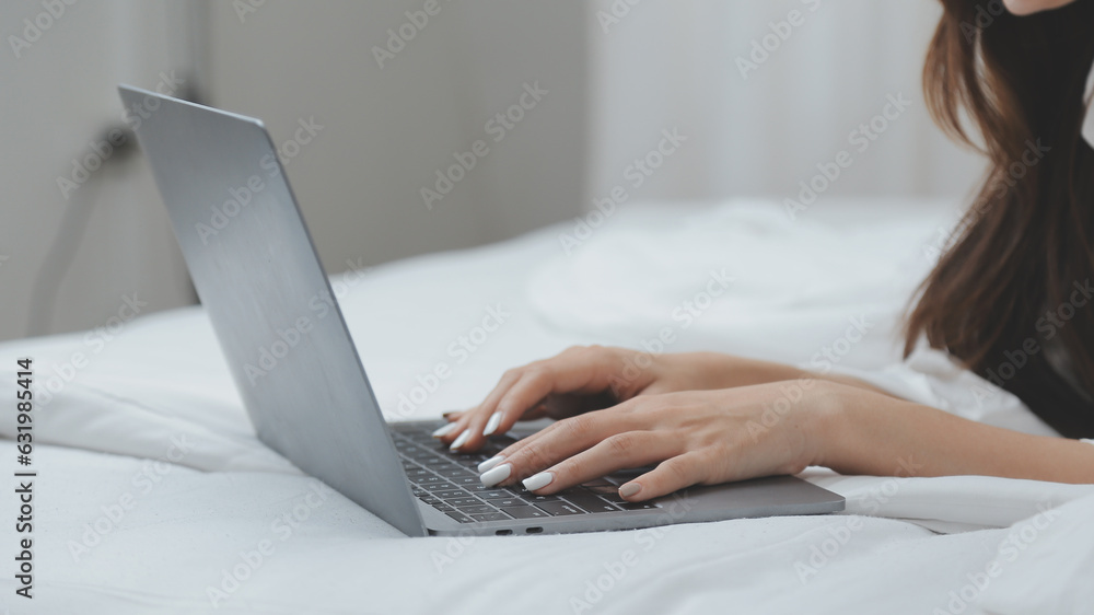 Naklejka premium Happy young female in casual clothes smiling and looking at camera while using laptop on bed in bedroom at home