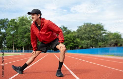 Young asian man wearing sportswear running outdoor. Portraits of Indian man stretching leg before running on the running track at sport stadium. Training athlete work out at outdoor concept.