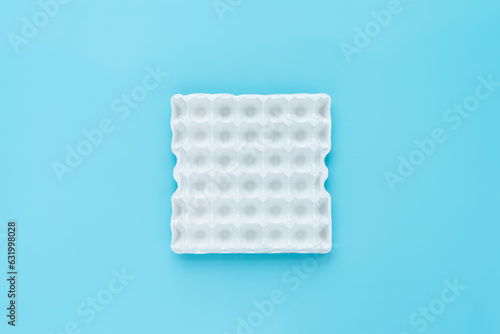 Still life of empty white egg carton for thirty eggs standing on turquoise surface, directly above view 
