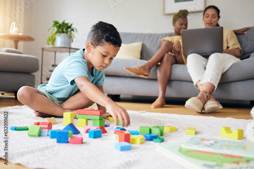Play, toys and child on floor with parents on sofa for learning, development and education. Lgbtq family, home and boy with building blocks for fun, relax and games with lesbian mothers on laptop