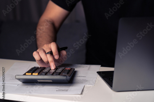Fototapeta Naklejka Na Ścianę i Meble -  Asian man is using a calculator to calculate his family's monthly miscellaneous expenses at home and record them in his laptop computer.