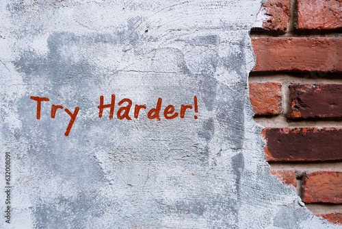 A grunge vintage brick wall and grey cement with hand written text TRY HARDER, concept of never give up and be persistent.