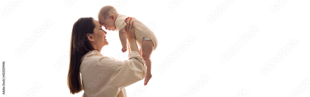 Mom tosses small daughter by white window and enjoys looking after infant in bedroom. Long haired mother happily playing with baby girl Mom tosses small daughter by white window and enjoys looking after infant in bedroom. Long haired mother happily playing with baby girl