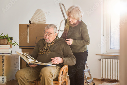 Senior couple looking at photo album surrounded by cardboard boxes in an empty room