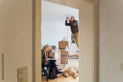 Senior couple in a new home with man mounting ceiling lamp photo