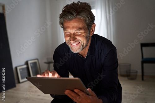 Portrait of smiling mature man having fun with digital tablet at home photo
