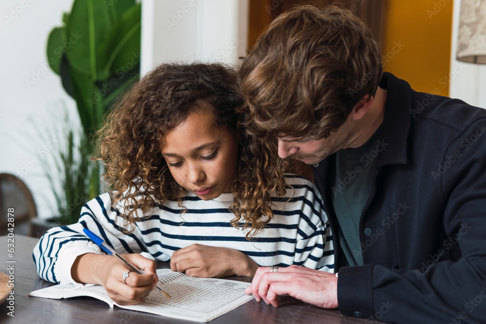 Father observing daughter solving a puzzle in a puzzle book Father observing daughter solving a puzzle in a puzzle book