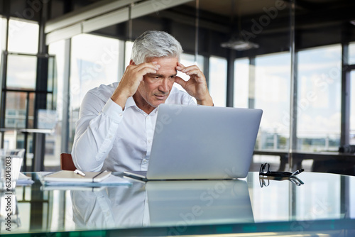 Stressed businessman sitting at desk with laptop, holding his head photo