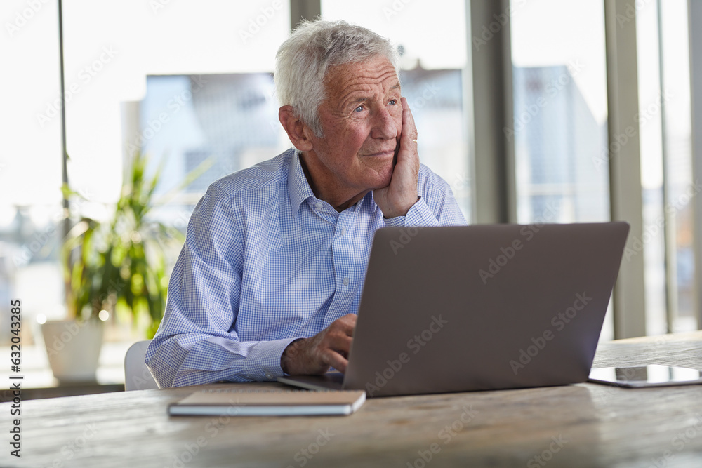 Portrait of pensive senior man sitting at table with laptop looking at distance Portrait of pensive senior man sitting at table with laptop looking at distance