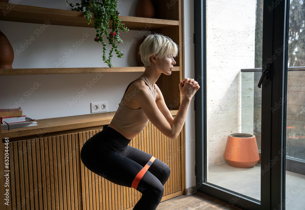 Blond woman doing squatting exercise at home Blond woman doing squatting exercise at home