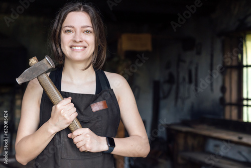 Billede på lærred Young woman blacksmith portrait with hammer in workshop